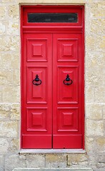 Image showing Bright red wooden door of a house with black doorknob rings