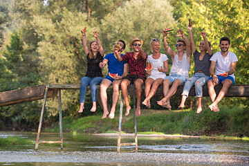 Image showing friends enjoying watermelon while sitting on the wooden bridge