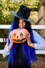 Image showing A girl in a witch costume with blue hair is holding a pumpkin with a painted face