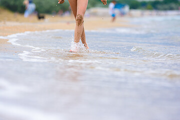 Image showing Close-up of the girl\'s feet soiled in the sand, the girl walks along the coastal strip towards the camera