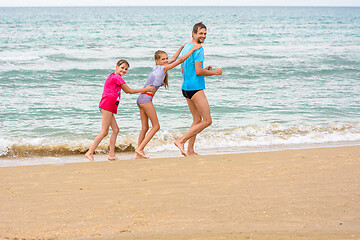 Image showing A man and two daughters are happily running along the beach with a train