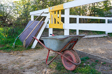 Image showing Old wheelbarrow in the background of the corral for horses, in the background there are shovels