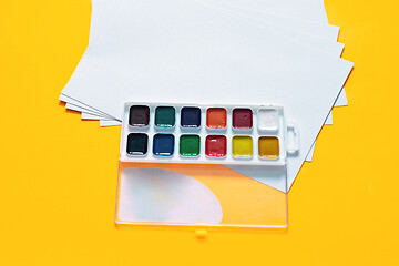 Image showing Blank white sheets and 12 colors of watercolor paint on a yellow background