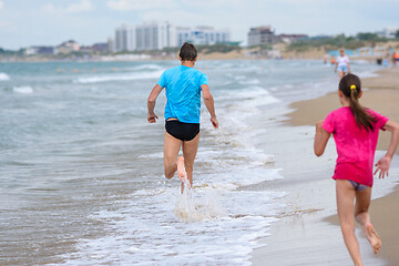 Image showing A man runs along the beach, a girl runs after him, rear view