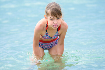 Image showing A girl stands knee-deep in sea water, grimaces and shows her tongue