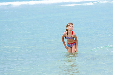 Image showing A girl stands knee-deep in sea water, does not want to go out to bask and sticks out her tongue