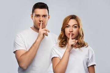 Image showing happy couple in white t-shirts making hush gesture