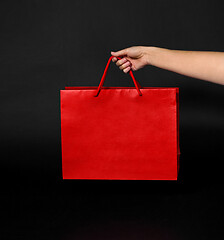 Image showing hand holding red shopping bag on black background