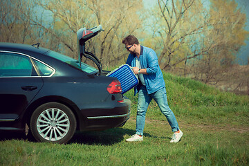 Image showing Handsome smiling man going to vacations, loading his suitcase in car trunk