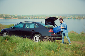 Image showing Handsome smiling man going to vacations, loading his suitcase in car trunk