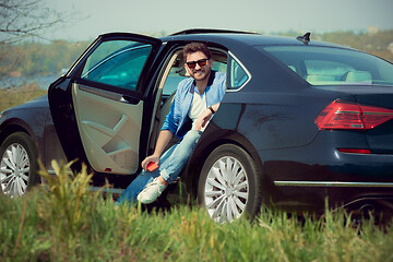 Image showing Handsome smiling man sitting in his car with opened doors