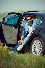 Image showing Handsome smiling man sitting in his car with opened doors