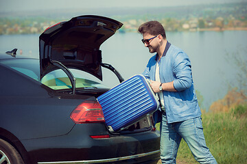 Image showing Handsome smiling man going to vacations, loading his suitcase in car trunk