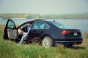 Image showing Handsome smiling man sitting in his car with opened doors