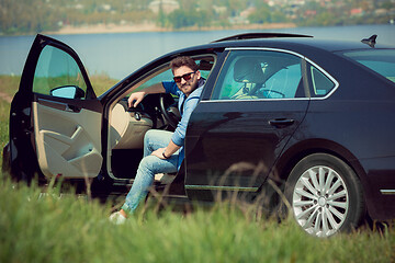 Image showing Handsome smiling man sitting in his car with opened doors