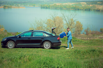 Image showing Handsome smiling man going to vacations, loading his suitcase in car trunk