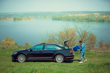 Image showing Handsome smiling man going to vacations, loading his suitcase in car trunk