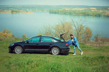 Image showing Handsome smiling man going to vacations, loading his suitcase in car trunk