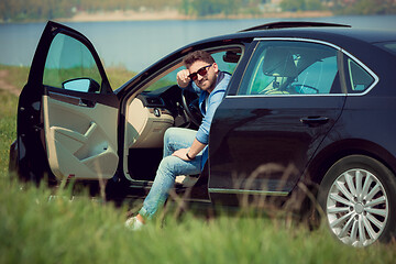 Image showing Handsome smiling man sitting in his car with opened doors