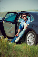 Image showing Handsome smiling man sitting in his car with opened doors