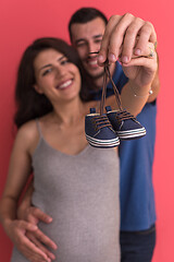 Image showing young pregnant couple holding newborn baby shoes