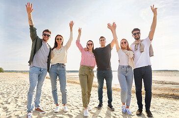 Image showing happy friends waving hands on beach in summer