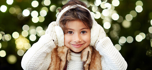 Image showing happy little girl in earmuffs over winter forest