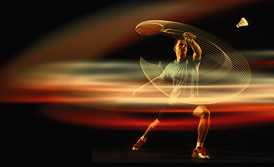 Image showing Young man playing badminton over dark background