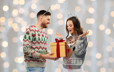 Image showing happy couple in ugly sweaters with christmas gift