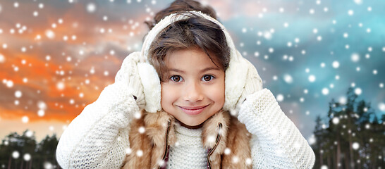 Image showing happy little girl in earmuffs over winter forest