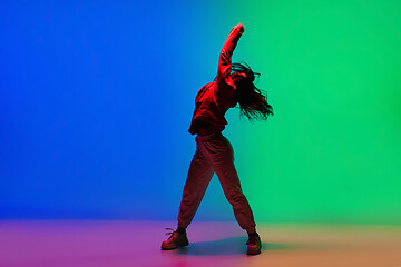 Image showing Stylish sportive girl dancing hip-hop in stylish clothes on colorful background at dance hall in neon light. Youth culture, movement, style and fashion, action.