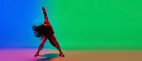 Image showing Stylish sportive girl dancing hip-hop in stylish clothes on colorful background at dance hall in neon light. Youth culture, movement, style and fashion, action.