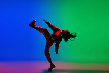 Image showing Stylish sportive girl dancing hip-hop in stylish clothes on colorful background at dance hall in neon light. Youth culture, movement, style and fashion, action.