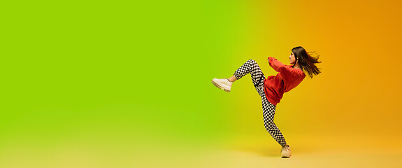 Image showing Stylish sportive girl dancing hip-hop in stylish clothes on colorful background at dance hall in neon light. Youth culture, movement, style and fashion, action.