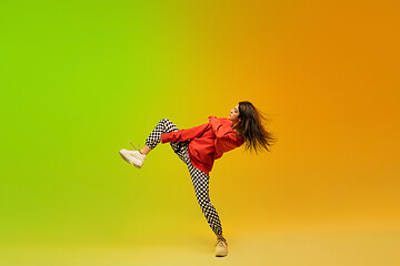 Image showing Stylish sportive girl dancing hip-hop in stylish clothes on colorful background at dance hall in neon light. Youth culture, movement, style and fashion, action.