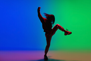 Image showing Stylish sportive girl dancing hip-hop in stylish clothes on colorful background at dance hall in neon light. Youth culture, movement, style and fashion, action.