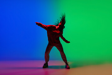 Image showing Stylish sportive girl dancing hip-hop in stylish clothes on colorful background at dance hall in neon light. Youth culture, movement, style and fashion, action.