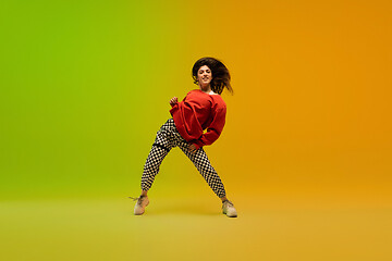 Image showing Stylish sportive girl dancing hip-hop in stylish clothes on colorful background at dance hall in neon light. Youth culture, movement, style and fashion, action.