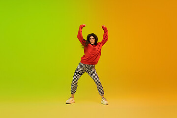 Image showing Stylish sportive girl dancing hip-hop in stylish clothes on colorful background at dance hall in neon light. Youth culture, movement, style and fashion, action.