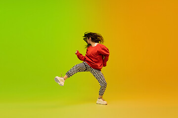 Image showing Stylish sportive girl dancing hip-hop in stylish clothes on colorful background at dance hall in neon light. Youth culture, movement, style and fashion, action.