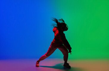 Image showing Stylish sportive girl dancing hip-hop in stylish clothes on colorful background at dance hall in neon light. Youth culture, movement, style and fashion, action.