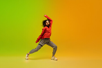 Image showing Stylish sportive girl dancing hip-hop in stylish clothes on colorful background at dance hall in neon light. Youth culture, movement, style and fashion, action.