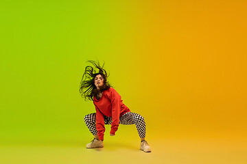 Image showing Stylish sportive girl dancing hip-hop in stylish clothes on colorful background at dance hall in neon light. Youth culture, movement, style and fashion, action.