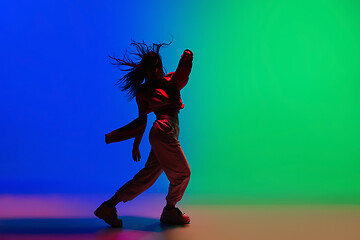 Image showing Stylish sportive girl dancing hip-hop in stylish clothes on colorful background at dance hall in neon light. Youth culture, movement, style and fashion, action.