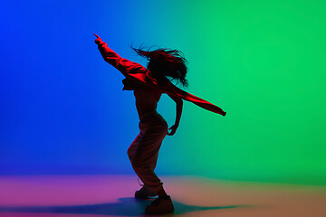 Image showing Stylish sportive girl dancing hip-hop in stylish clothes on colorful background at dance hall in neon light. Youth culture, movement, style and fashion, action.