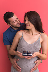 Image showing young pregnant couple holding newborn baby shoes