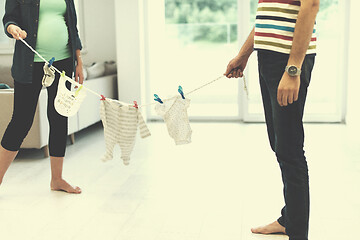 Image showing young couple holding baby bodysuits at home