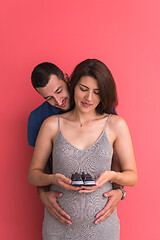 Image showing young pregnant couple holding newborn baby shoes