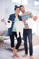 Image showing young couple holding baby bodysuits at home