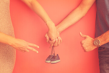 Image showing young pregnant couple holding newborn baby shoes